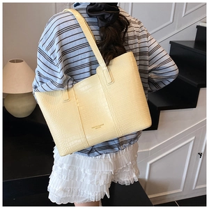 Detail of cream tote bag featuring crocodile pattern leather and long shoulder straps
