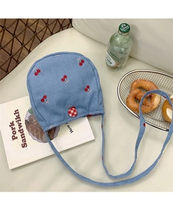 Détail du petit sac à bandoulière en denim bleu avec broderie de cerises et bouton