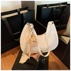 Detail of a beige crescent-shaped leather shoulder bag with a cute plush bear charm