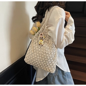 Close-up of cream woven macrame tote bag with decorative doll charm and mesh texture