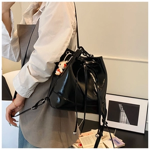 Detail of black glossy bucket bag with drawstring closure and a white rabbit plush charm