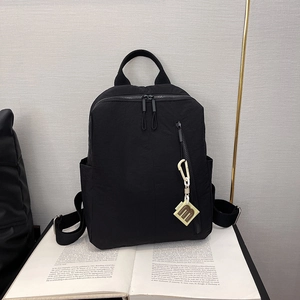 Detail of a black nylon backpack with a textured matte finish and a B-letter charm