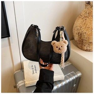 Close-up of black crescent hobo bag with a plush bear charm on a denim canvas texture