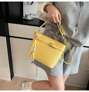 Detail of yellow lychee texture bucket bag featuring buckle strap and heart pendant charm