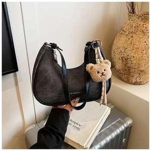 Detail of black denim hobo bag featuring leather trim and a cute plush bear pendant