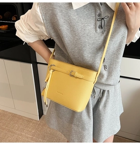 Detailed shot of yellow bucket bag with lychee texture and decorative tassel strap