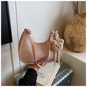 Pink suede underarm bag detail with plush bear charm and sleek gold metal brand logo