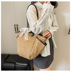 Détail du sac cabas en paille tissé avec anses en cuir noir et nœud en dentelle blanche