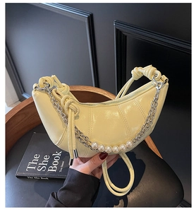 Detail of yellow crescent bag featuring pleated faux leather and pearl chain strap