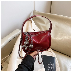 Detail of burgundy cylinder handbag with glossy leather finish and silver dog charm
