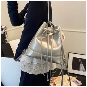 Detail of silver metallic bucket bag showing drawstring closure and bow accent on model
