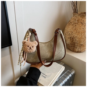 Detail of grey canvas hobo bag with brown leather strap and cute bear charm decoration
