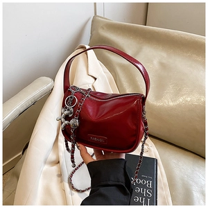 Detail of burgundy glossy pleated leather handbag with chain strap and fashion charm