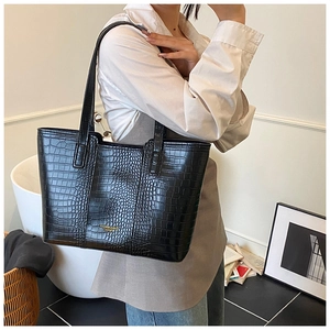 Detail of black crocodile pattern tote bag with gold lettering shown in a lifestyle setting