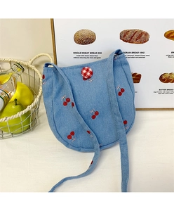 Détail du sac bandoulière en denim bleu clair avec broderie cerise et bouton vichy rouge