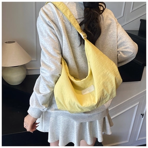 Detail of a bright yellow crescent nylon crossbody bag with textured fabric and woven label