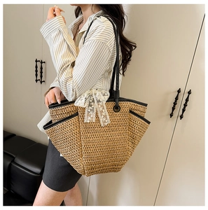 Détail du sac cabas en paille avec bordure en cuir noir et nœud en dentelle sur mannequin