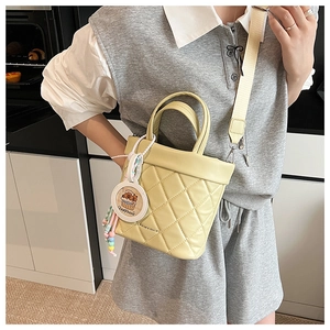 Detail of a quilted crossbody bucket bag with wide shoulder strap and cartoon charm