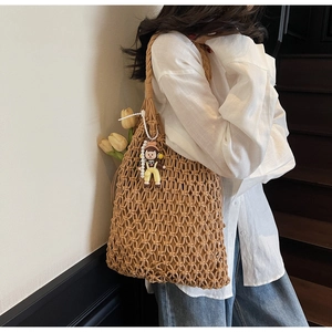 Close-up of camel hollow-out woven tote bag with a cute doll charm on a shoulder strap