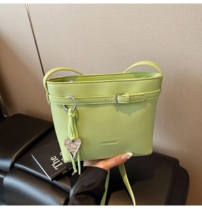 Detail of light green bucket bag with lychee texture, heart pendant, and tassel charm