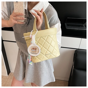 Close-up of yellow quilted handbag featuring diamond stitching and cute capybara charm