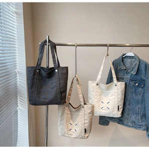 Detailed view of three canvas tote bags in gray and beige hanging on a metal rack