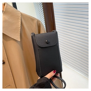 Detailed close-up of a black lychee texture mini phone bag held by hand in urban light