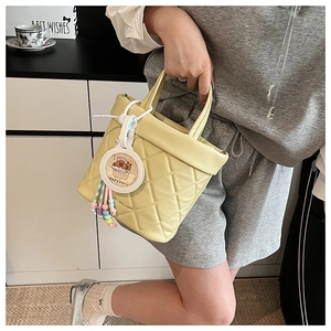 Detailed macro view of a pale yellow quilted bucket bag with a cute capybara pendant charm