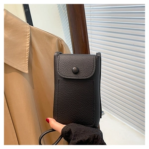 Detail of black litchi texture phone crossbody bag held by hand in a natural light setting