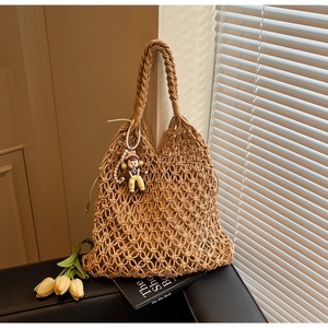 Detail of hand-woven khaki hollow tote bag with pearl charm and natural window light