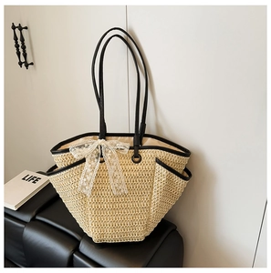 Détail d'un sac cabas en paille tissée avec bordure en cuir noir et nœud en dentelle