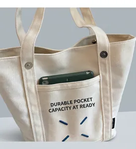 Detail of canvas tote bag showing reinforced front pocket with a green smartphone inside