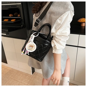 Detail of black quilted bucket bag with adjustable nylon strap and capybara charm