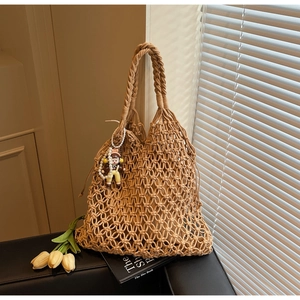 Detail of khaki handmade woven tote bag with hollow design and cute pearl doll pendant