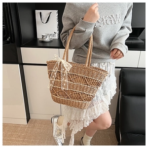 Detail view of woven straw tote bag featuring a large white lace bow and natural texture
