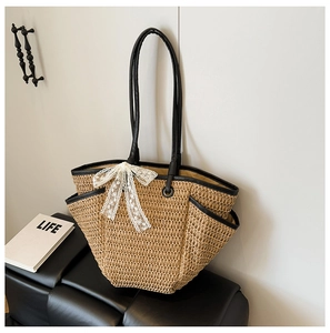 Détail du sac en paille avec poignées en cuir noir et un nœud décoratif en dentelle