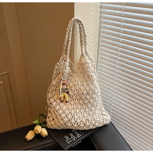 Detail of off-white hollow woven tote bag with a cute cartoon doll charm attachment