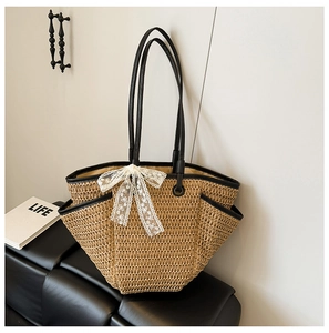 Détail du sac cabas en paille tressée avec bordure en cuir noir et nœud en dentelle blanche