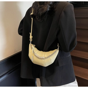 Detail of buttery yellow crescent bag with decorative pearl and silver chains on black blazer