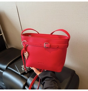 Detail of red bucket bag with litchi grain leather texture and heart metal charm