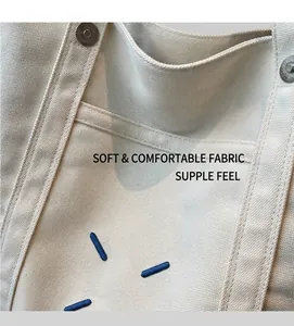 Detail of off-white canvas tote bag featuring metal rivet reinforcement and blue embroidery