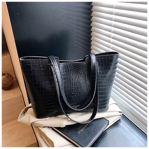 Detail of black crocodile texture tote bag with golden logo on a lifestyle background