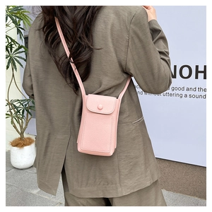 Close-up of pink litchi grain phone bag with snap closure on neutral suit outfit