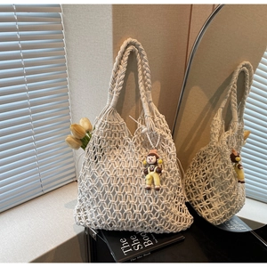 Detail showing the intricate hollow mesh weave and doll pendant on a beige tote bag