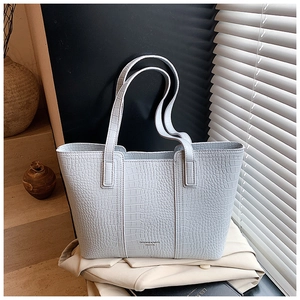 Close-up of light blue crocodile embossed tote bag texture with natural light and shadows