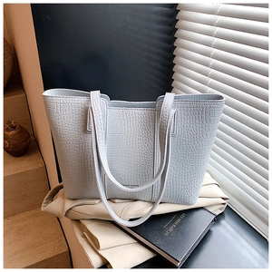 Detail of light blue crocodile-embossed tote bag styled with a blazer and book
