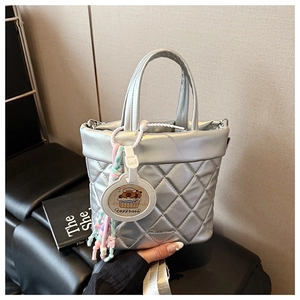 Macro shot of silver quilted shoulder bag with shiny metallic texture and capybara charm