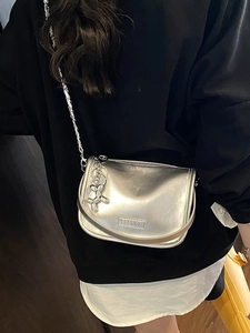 Silver metallic crossbody bag with chain strap and fashion label on a white dress