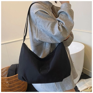 Minimalist black canvas hobo bag with wide shoulder strap worn by model in a clean room