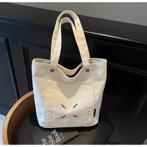 Detail of off-white canvas tote bag featuring unique blue X-shaped embroidery and side logo